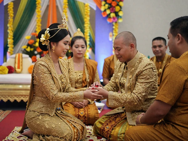 Traditional Cambodian Khmer wedding ceremony with couple in elegant gold-embroidered attire receiving Buddhist blessings